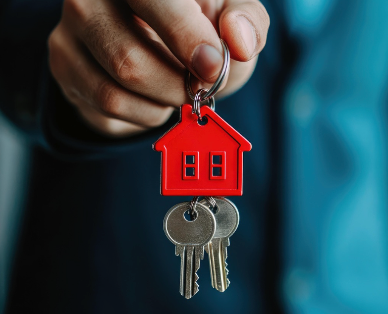 Una persona que sostiene un juego de llaves de casa con un llavero rojo con forma de casa, lo que simboliza el alquiler o la mudanza a una nueva vivienda.